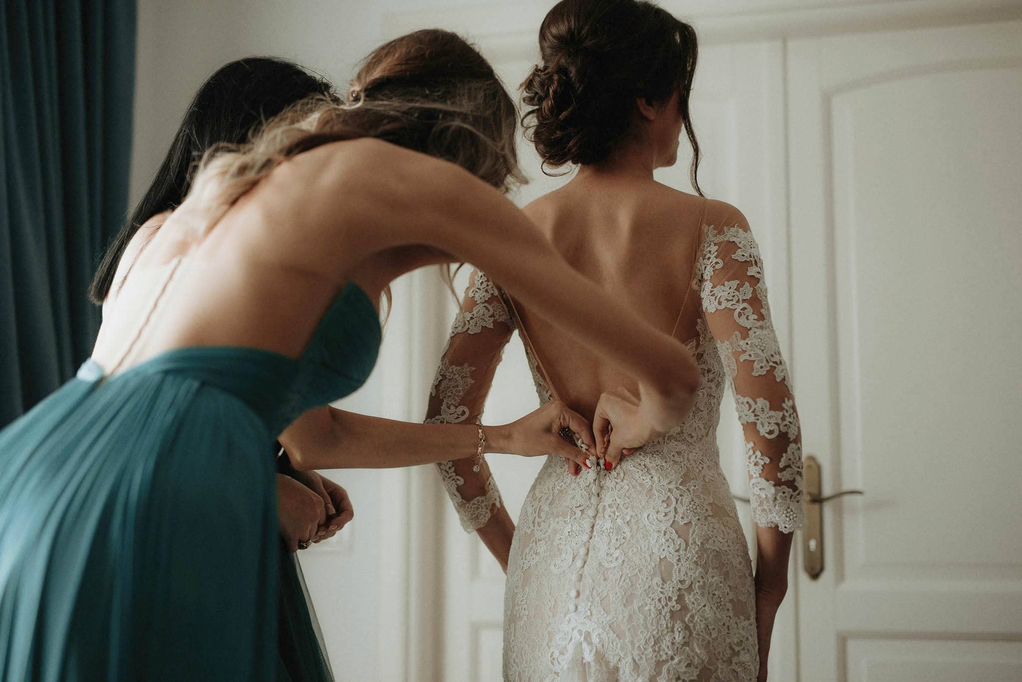 bridesmaid helps close the bride's dress back buttons