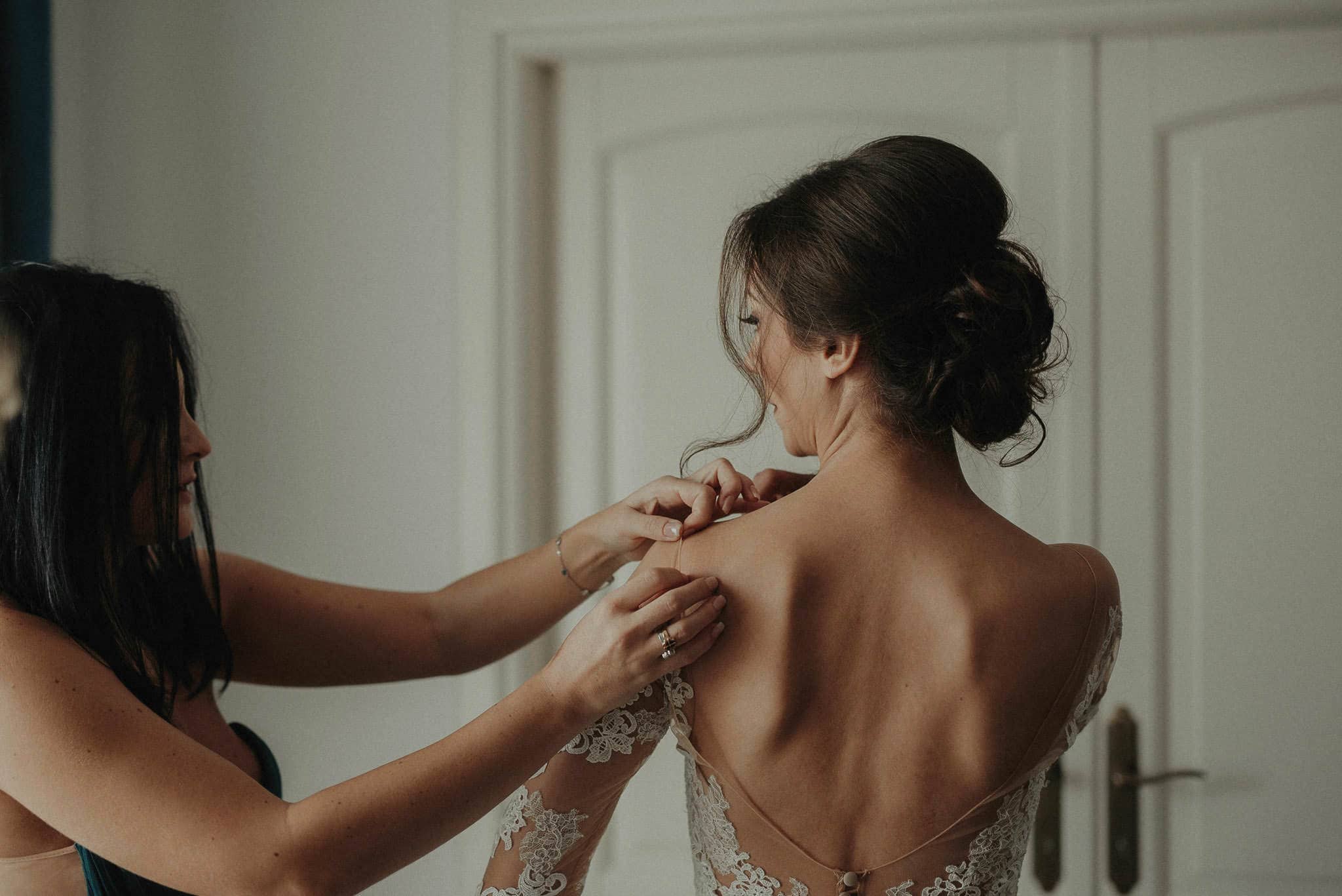 bridesmaid is helping the bride to put on her wedding dress