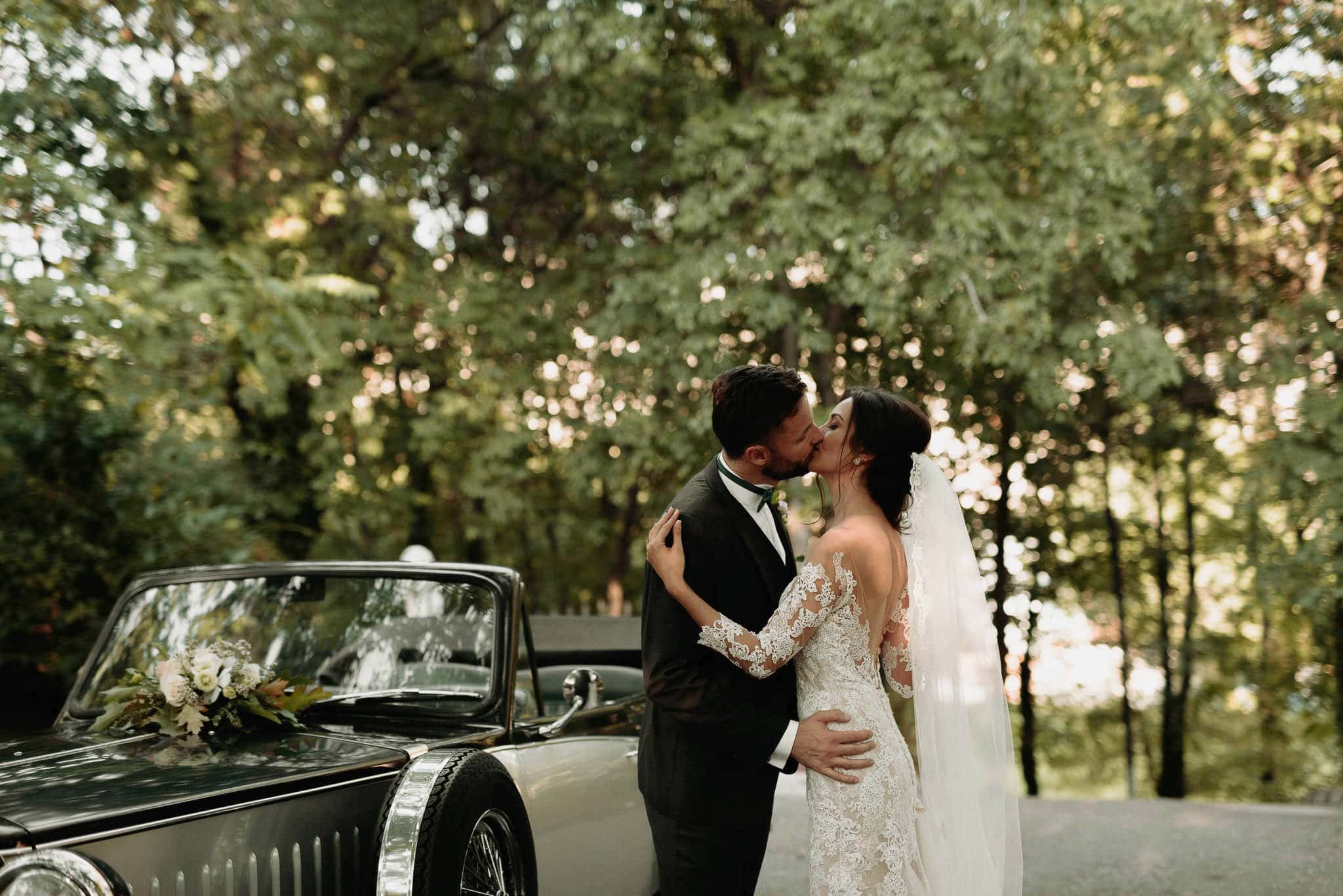 bride and groom during their photoshoot sharing a kiss next to their rented classical car