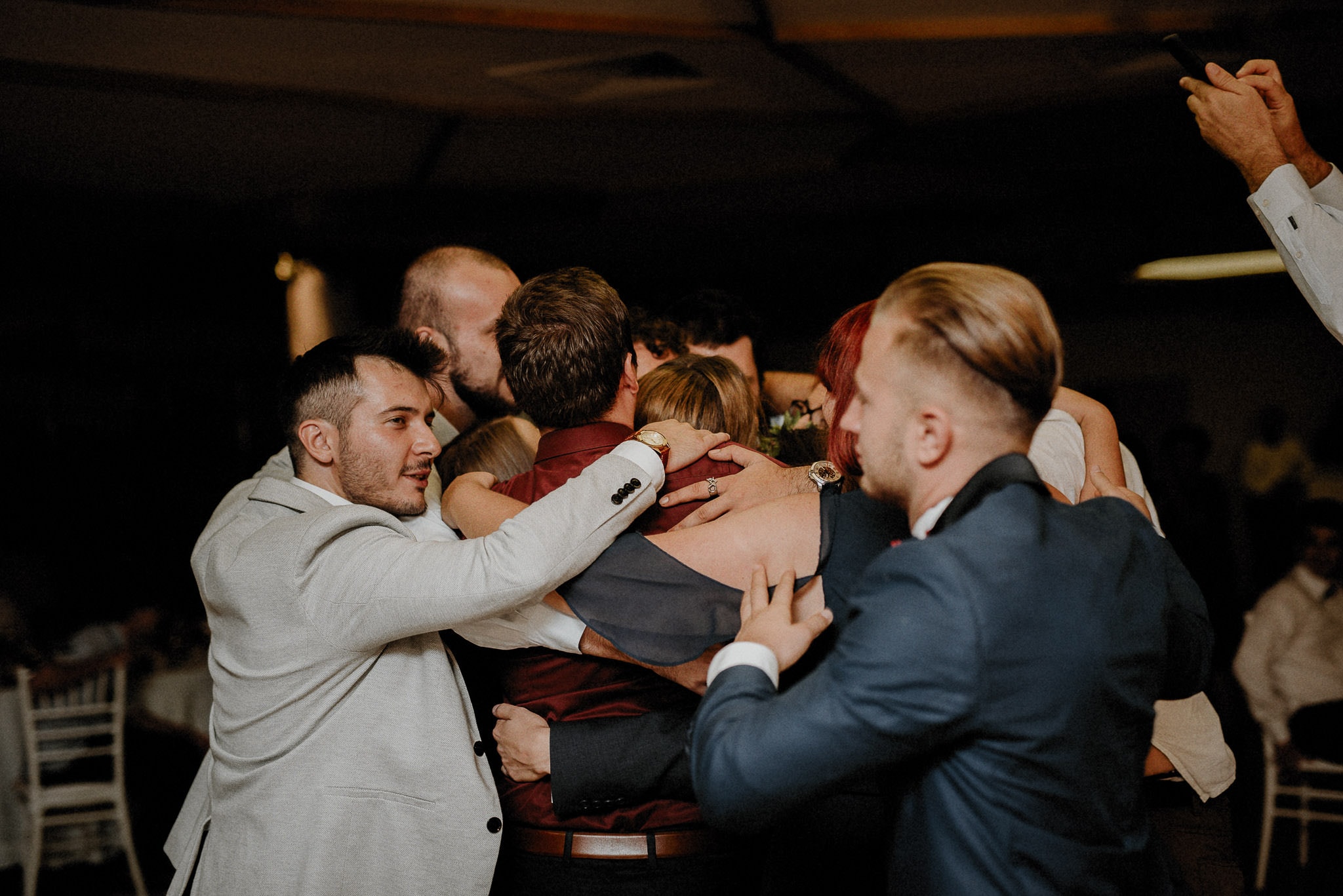 bride and groom are surrounded by all their friends in a group hug