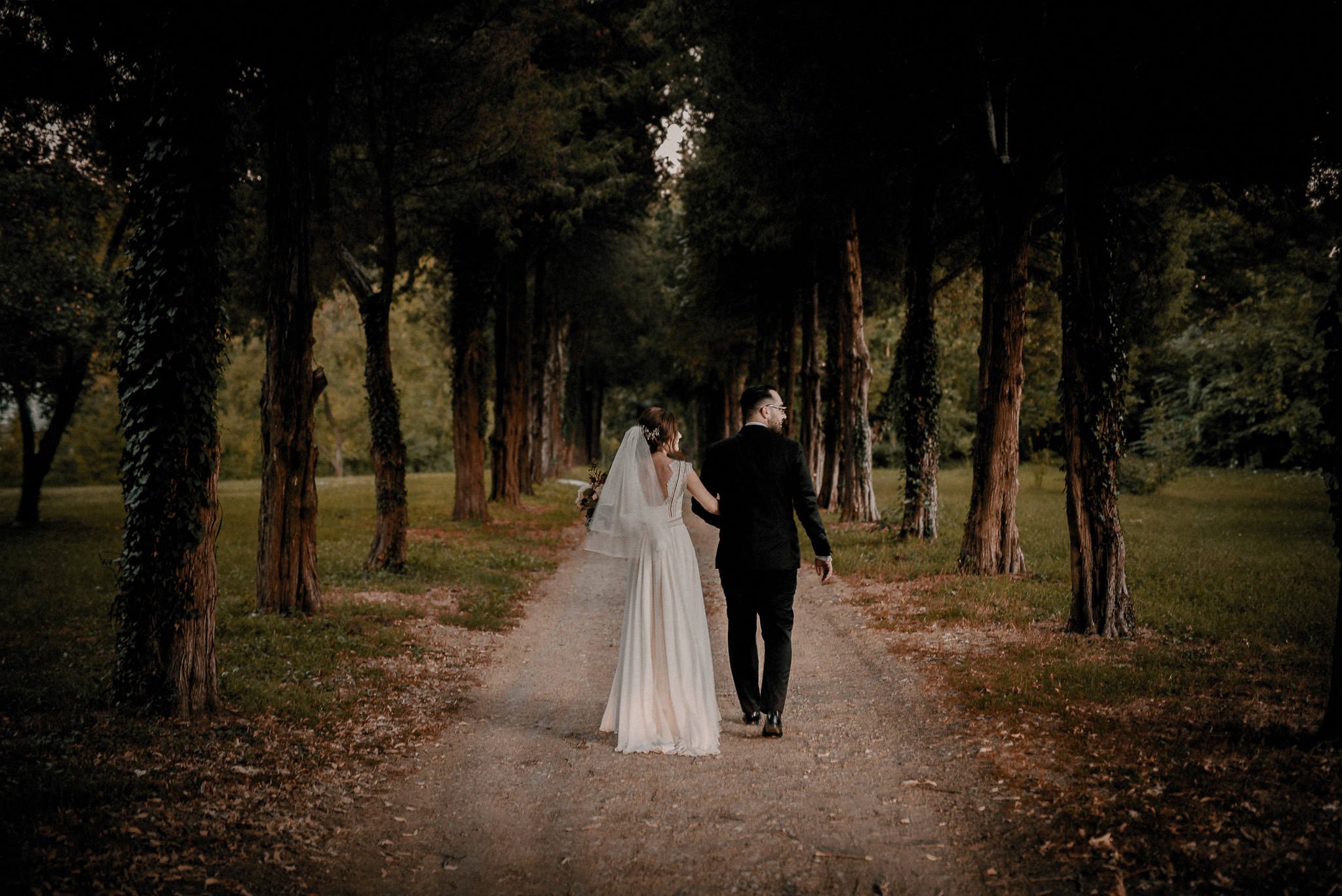 bride and groom walk down together surrounded by trees and nature during their intimate garden wedding