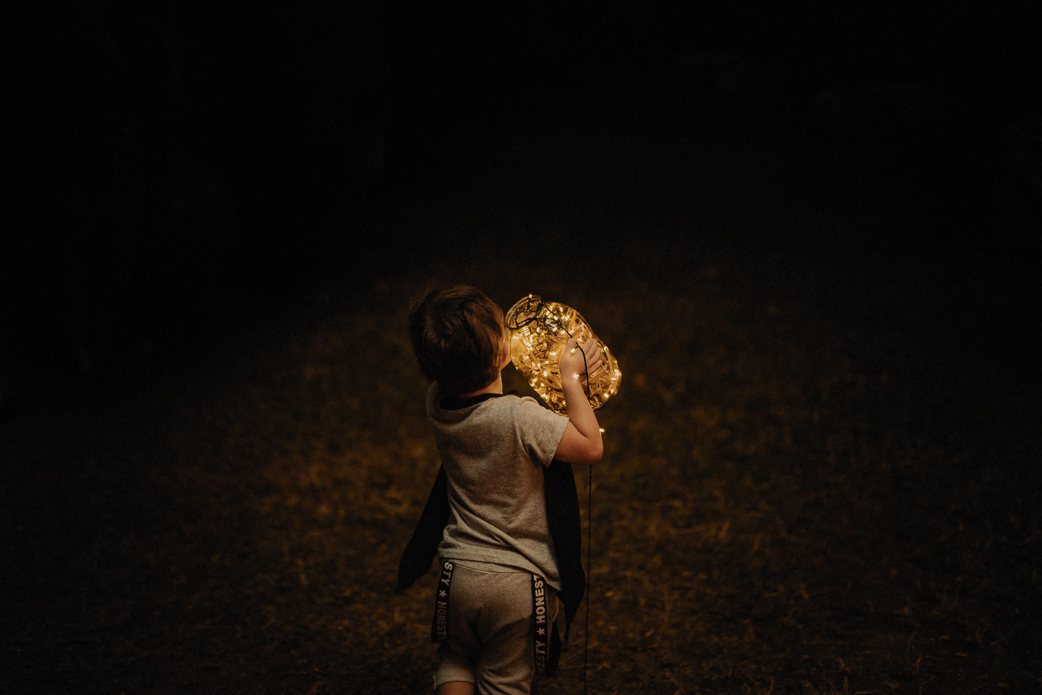 little boy carrying jar with fairy lights during forest wedding