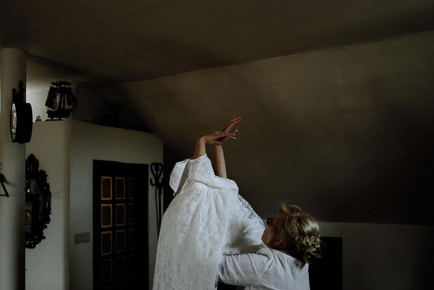 Charming Destination Wedding in the Portuguese Countryside - bride gets help from her mother to put her wedding dress on detail showing expressive hands in a moody environment