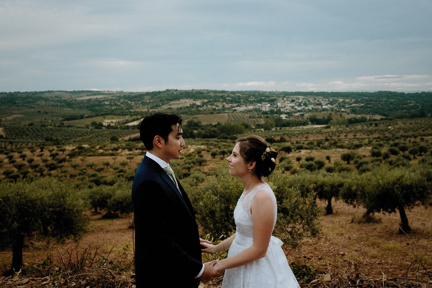 Charming Destination Wedding in the Portuguese Countryside - bride and groom looking at each other with the hilly landscape and olive trees behind them
